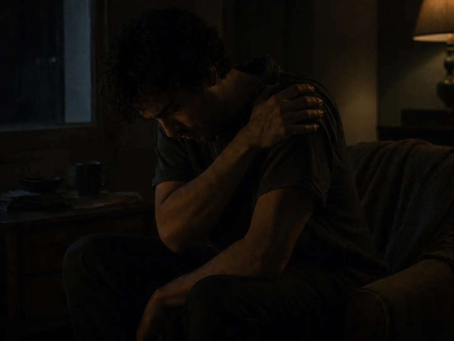 Silhouette assise dans l’ombre tenant son épaule dans une ambiance de douleur contenue